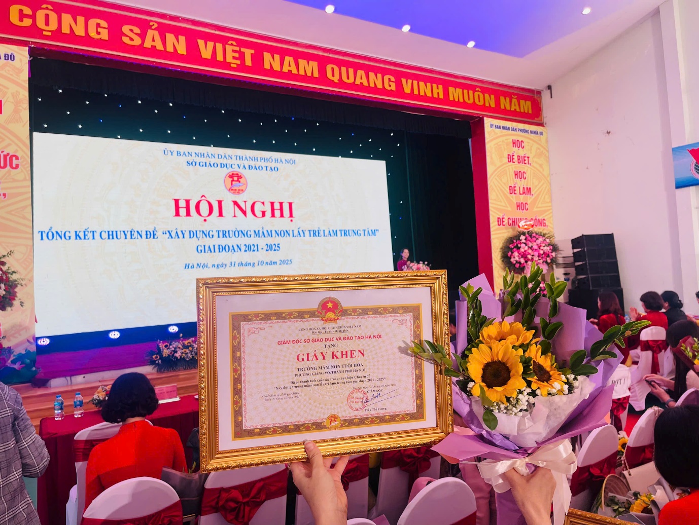 A person holding a picture frame and flowers in front of a screen

AI-generated content may be incorrect.