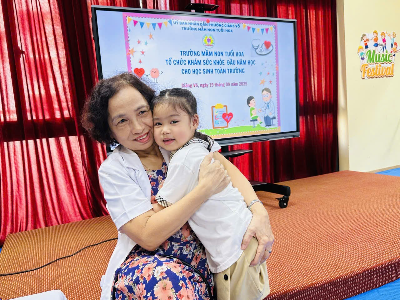 A person hugging a child in front of a screen

Description automatically generated