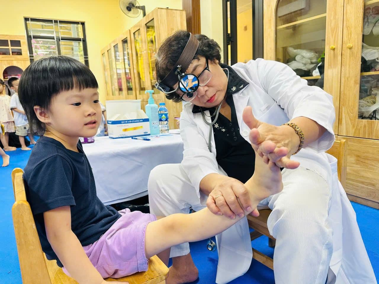 A person in a white coat and glasses holding a child's leg

Description automatically generated