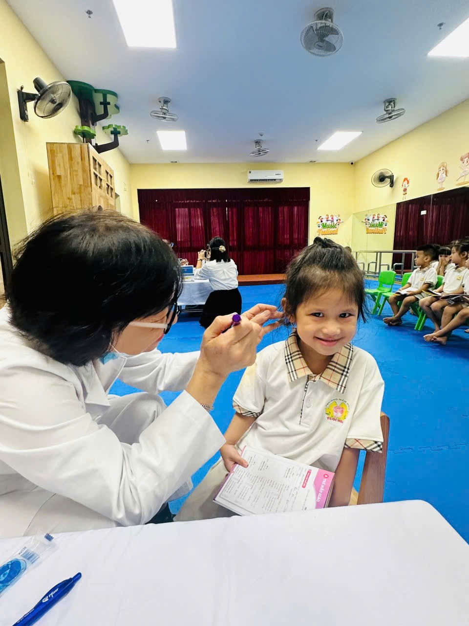A person in a white coat holding a child's ear

Description automatically generated