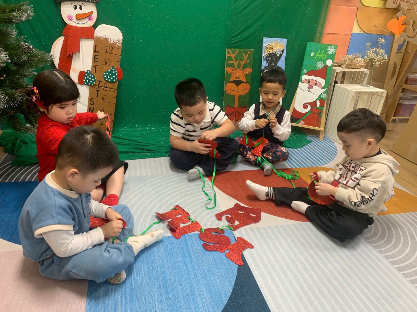 Hính ảnh các bé cùng nhau xâu dây chữ Merry Christmas rất tập trung